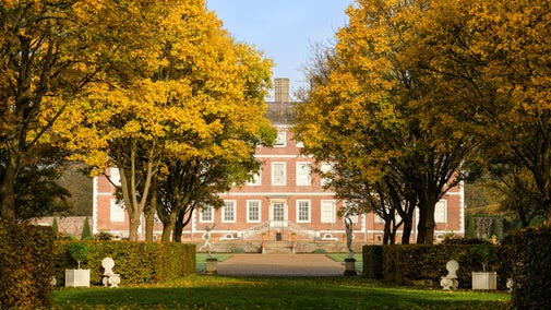 South front of the house from the Wilderness at Ham House and Garden, London. Two avenues of golden-leaved trees with statuary beneath, lead towards the red-brick Ham House with its external double staircase
